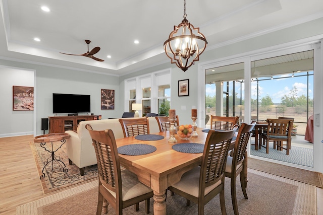 dining area featuring ceiling fan with notable chandelier, a raised ceiling, and light wood-type flooring