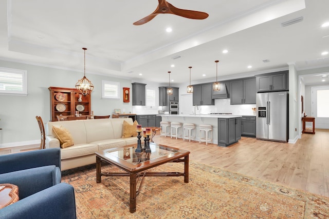 living room featuring a tray ceiling, a wealth of natural light, light hardwood / wood-style flooring, and ceiling fan with notable chandelier