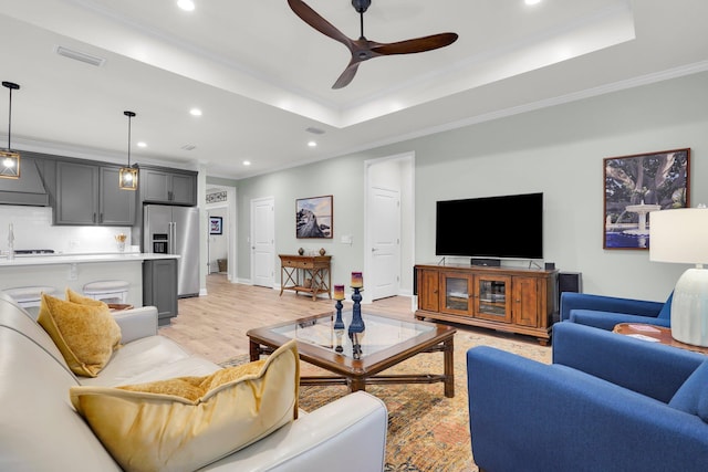 living room with a raised ceiling, sink, ceiling fan, light wood-type flooring, and ornamental molding