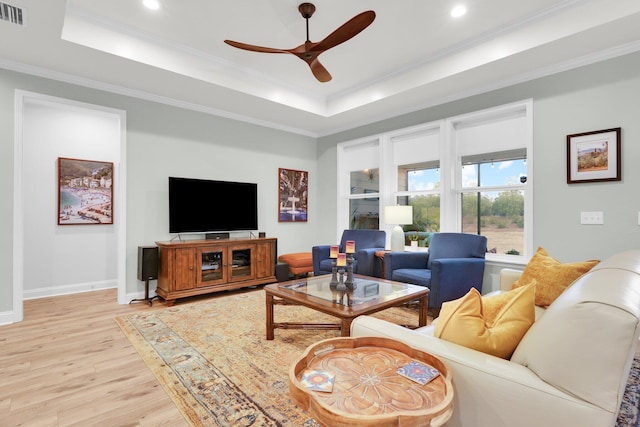 living room featuring ceiling fan, a raised ceiling, light wood-type flooring, and crown molding