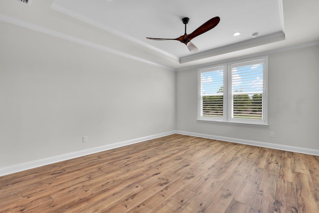empty room with baseboards, a raised ceiling, a ceiling fan, crown molding, and wood-type flooring