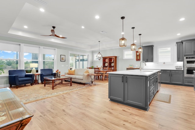 kitchen with gray cabinets, a kitchen island with sink, a tray ceiling, and sink