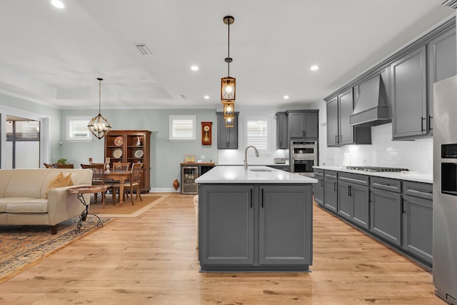 kitchen featuring custom exhaust hood, sink, decorative light fixtures, gray cabinets, and an island with sink