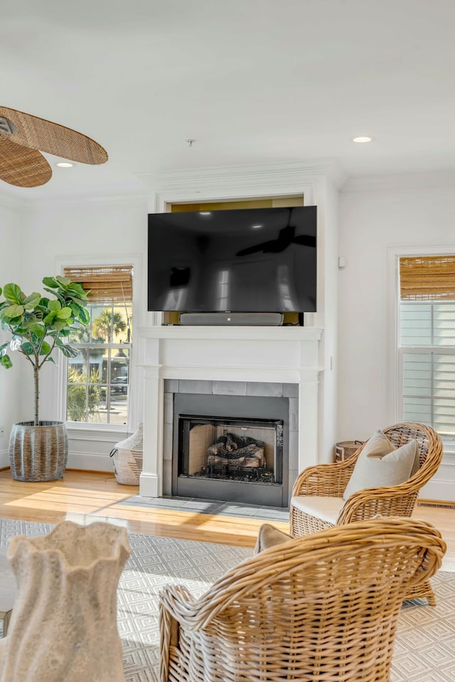 living area with crown molding, a ceiling fan, a fireplace, and wood finished floors