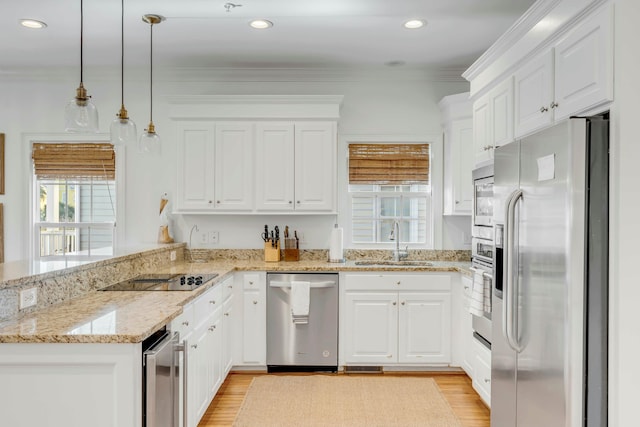 kitchen with white cabinets, a peninsula, stainless steel appliances, crown molding, and a sink