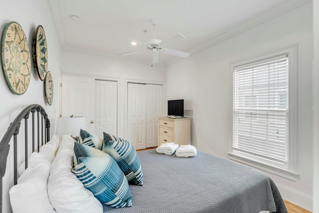 bedroom with multiple closets, a ceiling fan, ornamental molding, wood finished floors, and baseboards