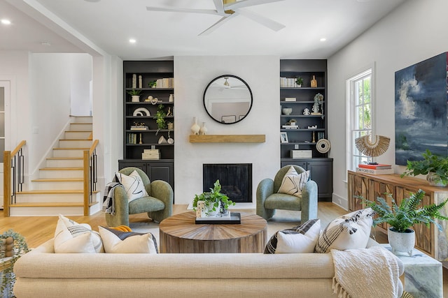 living room with built in shelves, light hardwood / wood-style floors, and ceiling fan