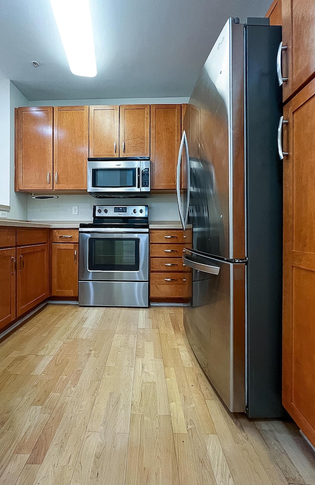 kitchen with light countertops, appliances with stainless steel finishes, brown cabinetry, and light wood-style flooring