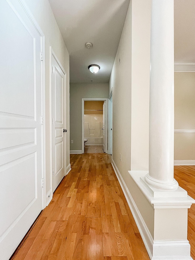 hall with baseboards, decorative columns, and light wood finished floors