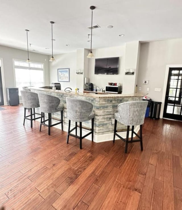 kitchen with dark wood-style floors, a kitchen bar, visible vents, and a healthy amount of sunlight