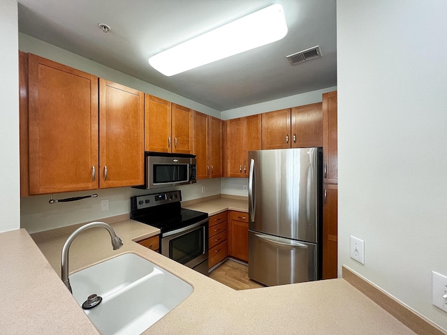 kitchen with a sink, visible vents, light countertops, appliances with stainless steel finishes, and brown cabinetry