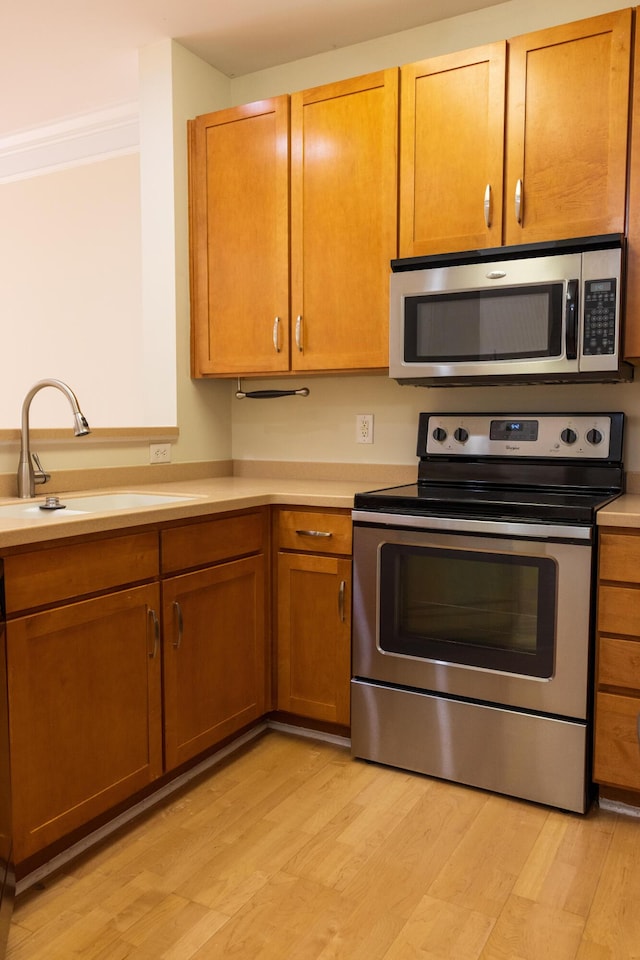 kitchen with stainless steel appliances, a sink, light wood-style floors, light countertops, and ornamental molding