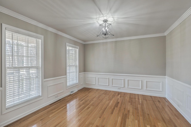 unfurnished room with a wainscoted wall, crown molding, visible vents, an inviting chandelier, and light wood-style floors