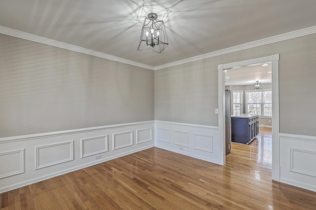 spare room featuring a chandelier, a decorative wall, a wainscoted wall, wood-type flooring, and crown molding