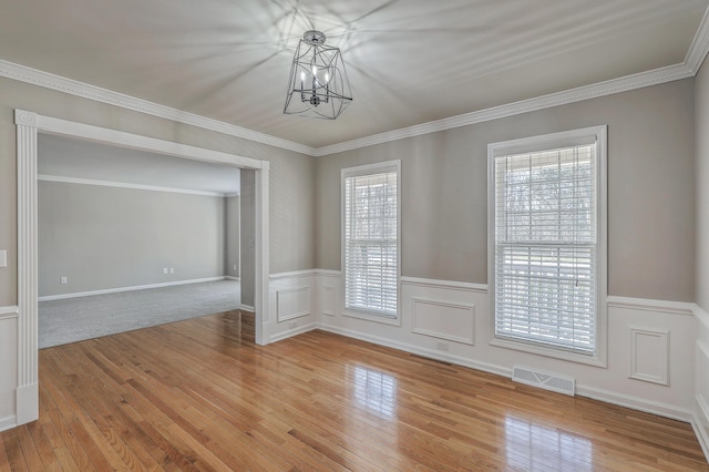 spare room featuring a chandelier, visible vents, wainscoting, light wood finished floors, and crown molding