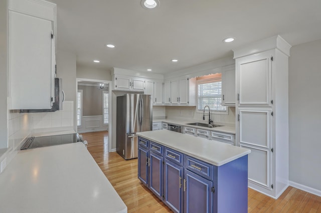 kitchen with light wood-style flooring, appliances with stainless steel finishes, light countertops, blue cabinetry, and a sink