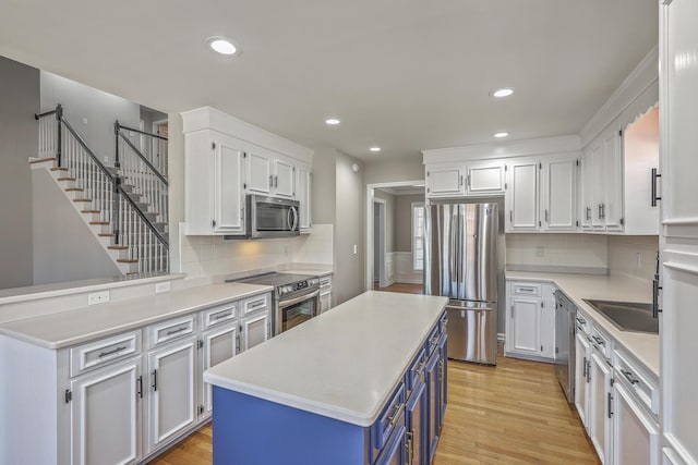 kitchen with blue cabinetry, stainless steel appliances, light wood-style flooring, white cabinets, and a sink