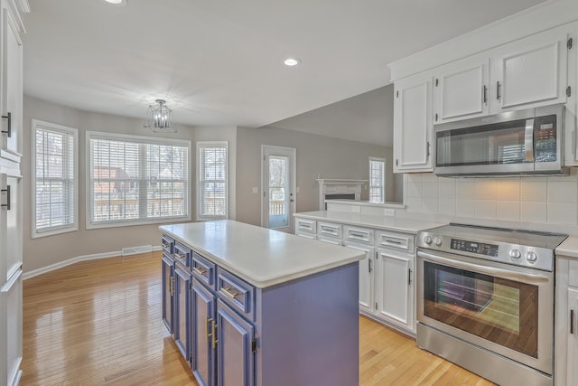 kitchen featuring blue cabinets, stainless steel appliances, a fireplace, white cabinets, and light countertops