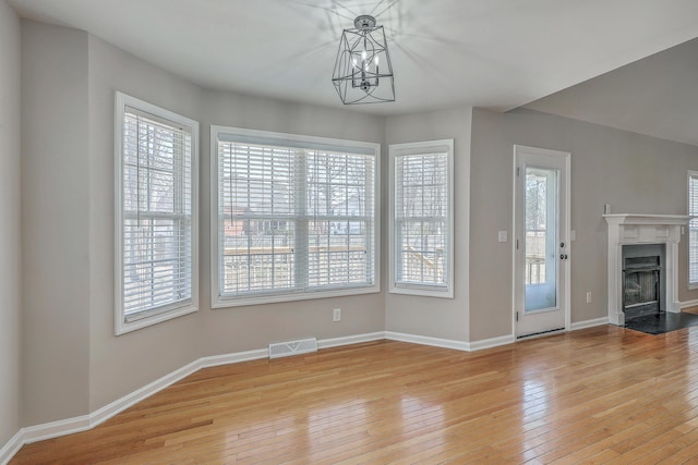 unfurnished dining area featuring wood-type flooring, a fireplace with flush hearth, visible vents, and baseboards