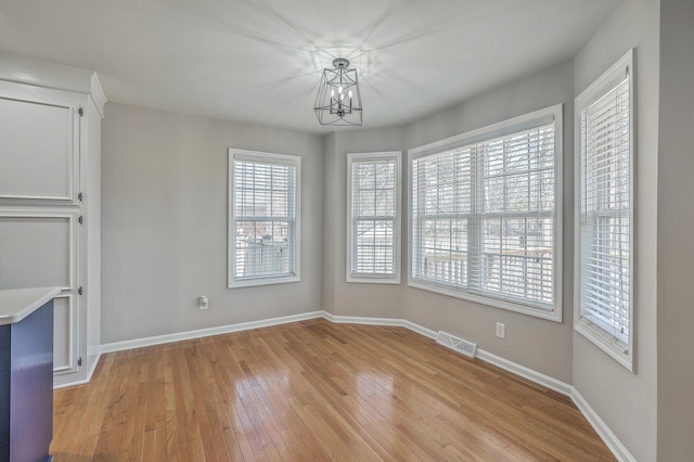 unfurnished dining area with light wood-style floors, visible vents, baseboards, and an inviting chandelier