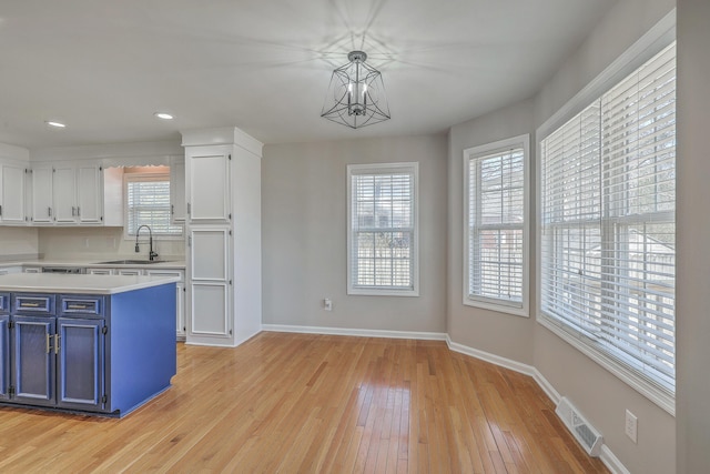 kitchen with light wood finished floors, light countertops, blue cabinetry, white cabinetry, and a sink