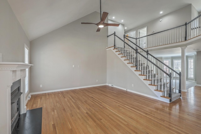 unfurnished living room featuring wood-type flooring, stairs, a high ceiling, and a fireplace with flush hearth