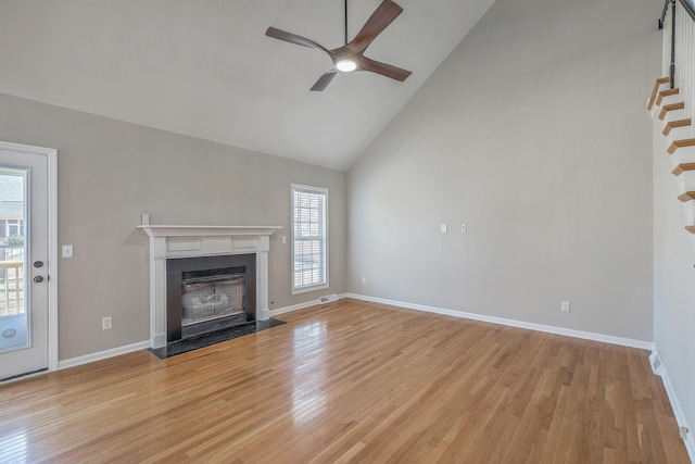 unfurnished living room with high vaulted ceiling, light wood-style flooring, a fireplace with flush hearth, baseboards, and stairs