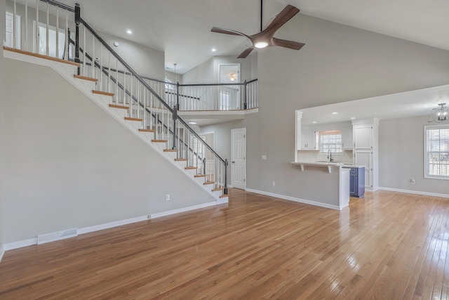 unfurnished living room with light wood finished floors, baseboards, visible vents, stairway, and high vaulted ceiling