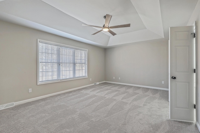 spare room with a raised ceiling, light colored carpet, visible vents, a ceiling fan, and baseboards