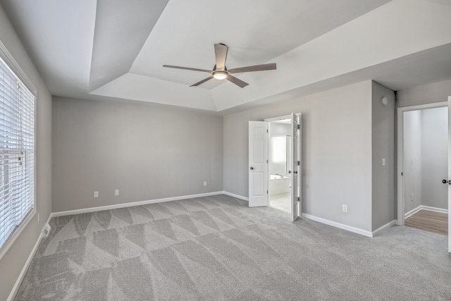 unfurnished bedroom with ceiling fan, baseboards, a raised ceiling, carpet, and ensuite bath