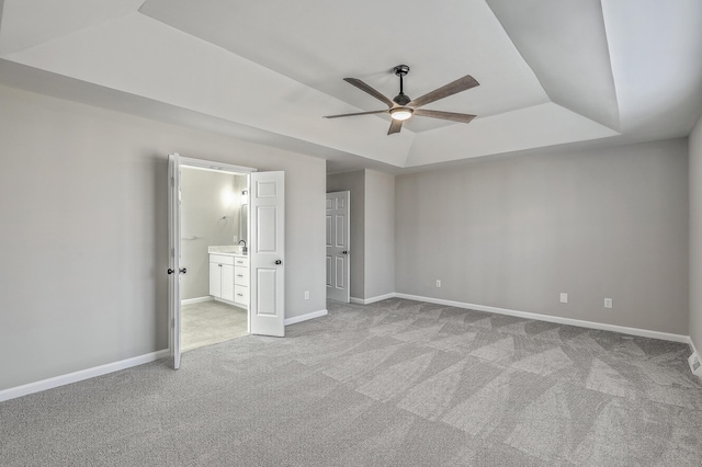 unfurnished bedroom with a tray ceiling, light colored carpet, ensuite bathroom, a ceiling fan, and baseboards