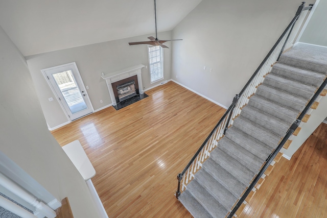 living room with high vaulted ceiling, a fireplace with flush hearth, baseboards, stairs, and light wood-type flooring