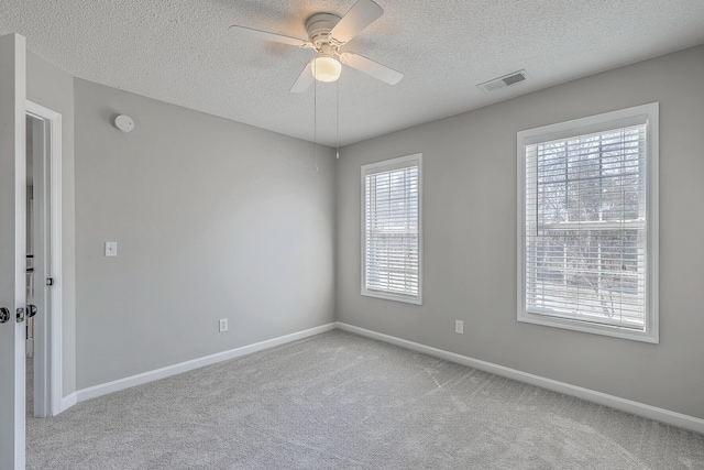 carpeted spare room with a ceiling fan, visible vents, a textured ceiling, and baseboards