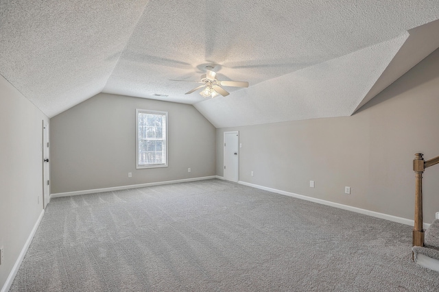 additional living space with baseboards, a ceiling fan, vaulted ceiling, a textured ceiling, and carpet floors