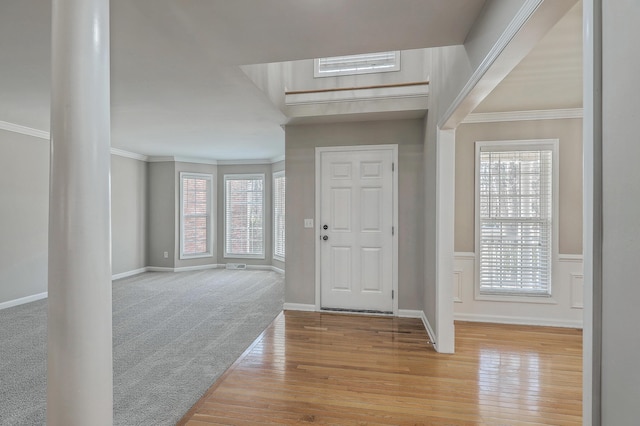 carpeted entrance foyer with baseboards, a wainscoted wall, wood finished floors, and crown molding