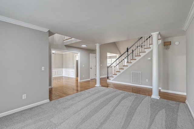 carpeted spare room featuring visible vents, wood finished floors, stairs, and decorative columns