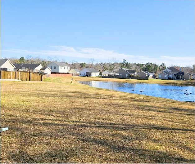 view of yard featuring a residential view, a water view, and fence