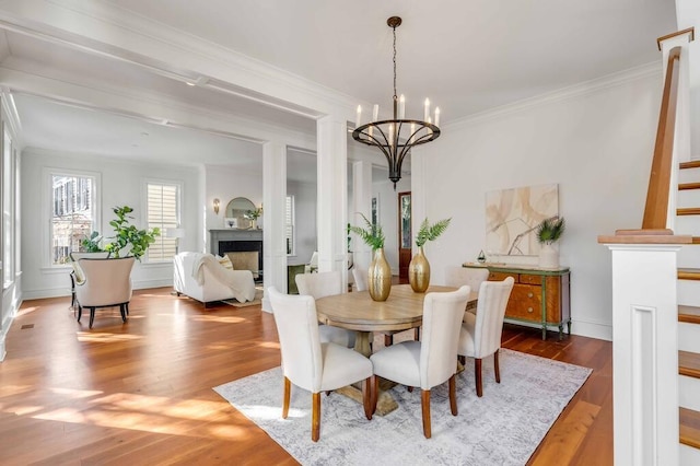 dining space with ornamental molding, stairway, wood finished floors, an inviting chandelier, and a fireplace