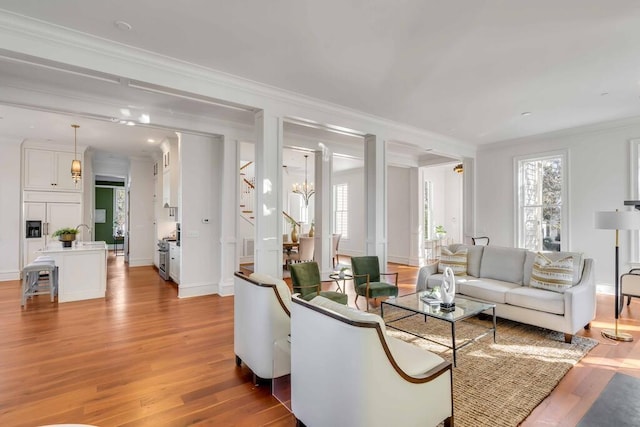 living room with ornamental molding, light wood-type flooring, stairway, and an inviting chandelier