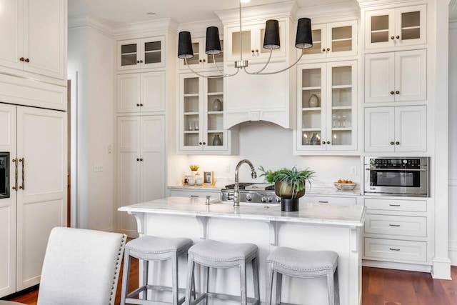 kitchen featuring a kitchen island with sink, oven, glass insert cabinets, and pendant lighting