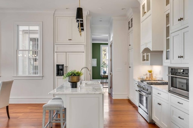 kitchen featuring pendant lighting, stainless steel appliances, glass insert cabinets, a sink, and an island with sink