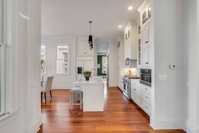 kitchen with a breakfast bar, stainless steel appliances, glass insert cabinets, white cabinets, and an island with sink