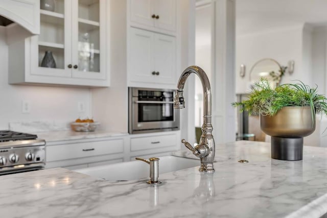 kitchen featuring stainless steel appliances, glass insert cabinets, white cabinets, and light stone counters