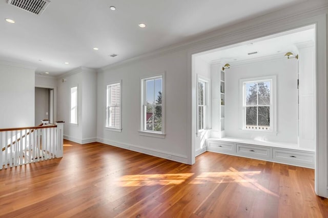 unfurnished room with baseboards, light wood finished floors, visible vents, and crown molding