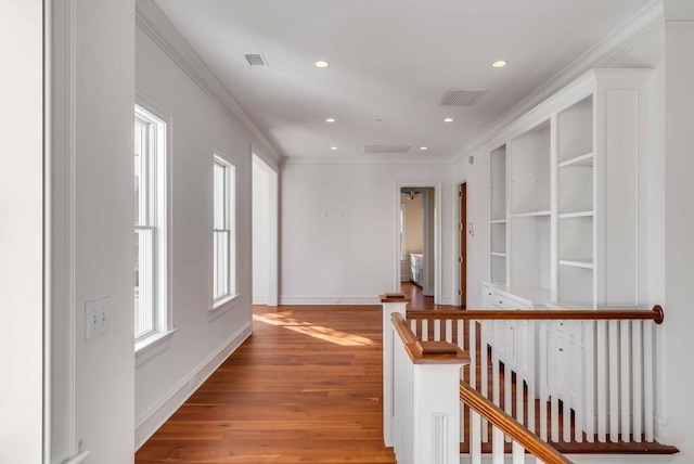 hallway featuring a healthy amount of sunlight, light wood-type flooring, ornamental molding, and an upstairs landing