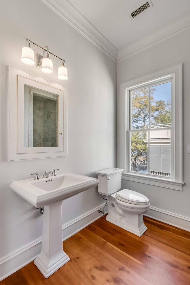 bathroom with toilet, ornamental molding, wood finished floors, and visible vents