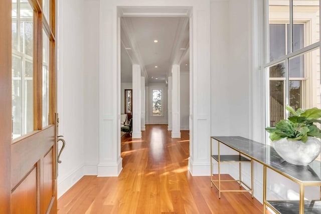 entryway with ornate columns, light wood-style flooring, ornamental molding, and a decorative wall