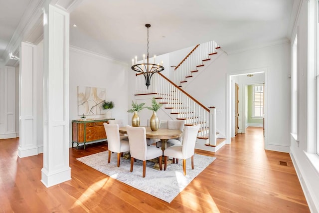 dining area with crown molding, decorative columns, an inviting chandelier, light wood-type flooring, and stairs