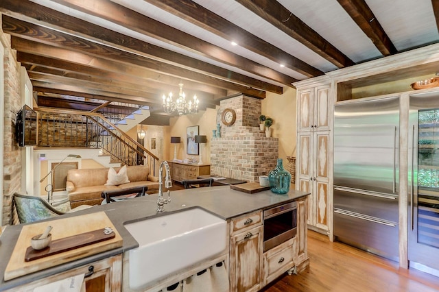 kitchen featuring sink, stainless steel built in fridge, a notable chandelier, beam ceiling, and light hardwood / wood-style floors