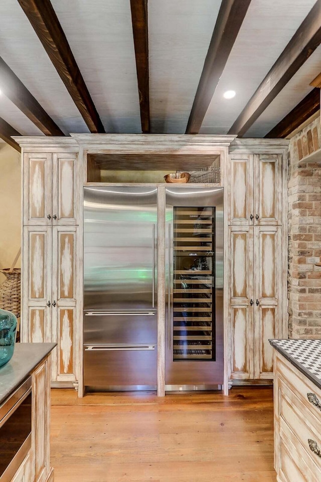 kitchen featuring built in appliances, light hardwood / wood-style floors, and beamed ceiling